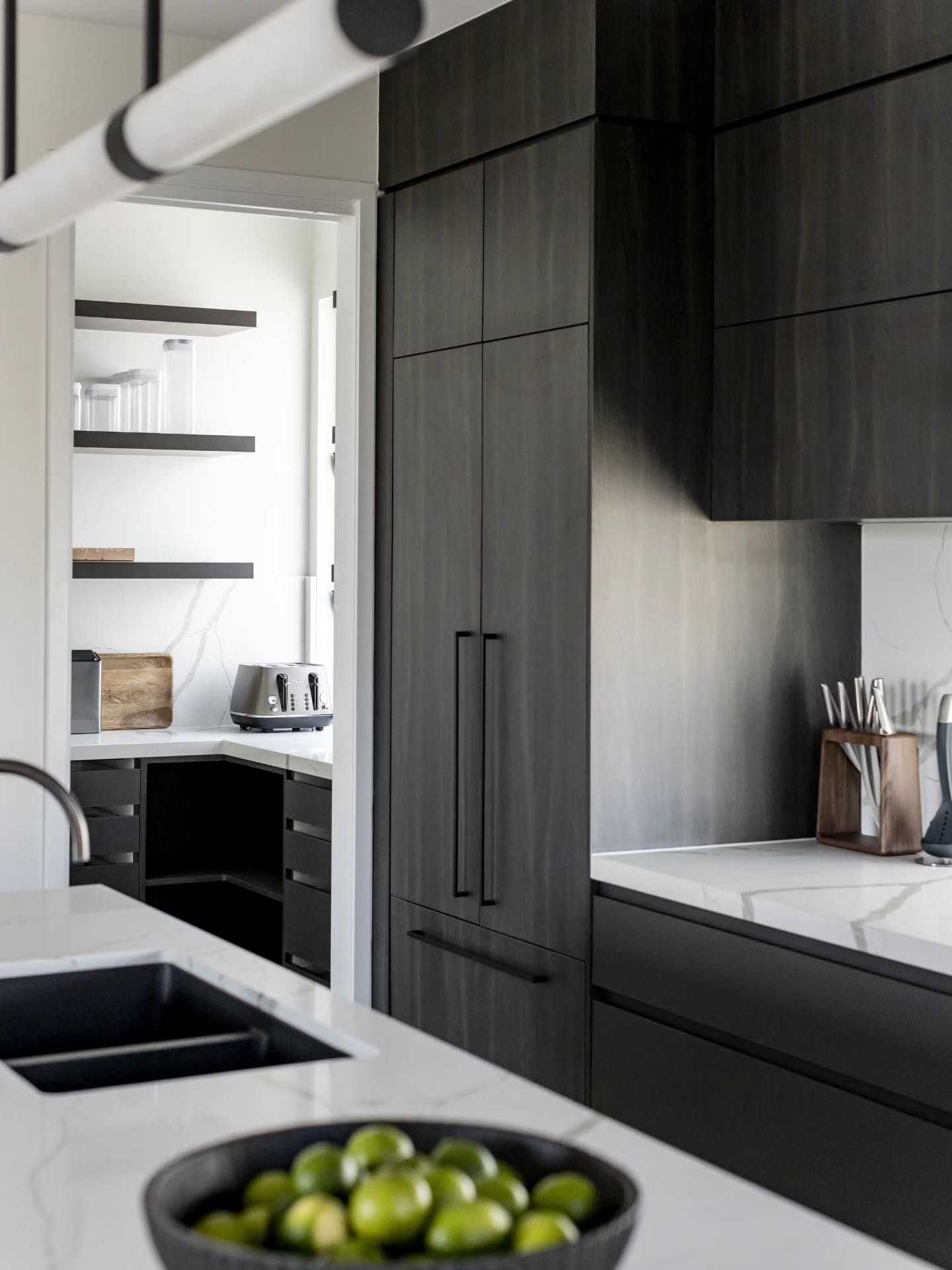 Dark stained timber kitchen cabinetry with the butler’s pantry visible beyond — Monochrome Residence