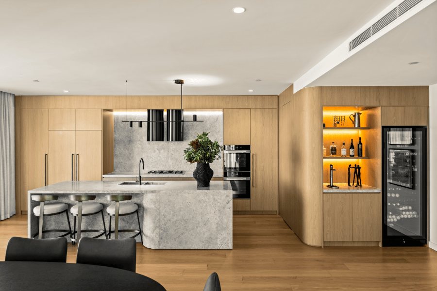 Kitchen with a marble waterfall island, timber cabinetry and a backlit integrated bar nook — Oceanside