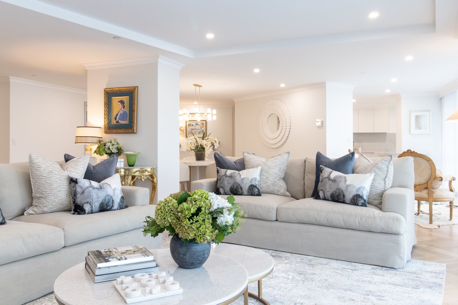 Open-plan living and dining with putty sofas, a round marble coffee table and a gold-framed portrait — Rivage