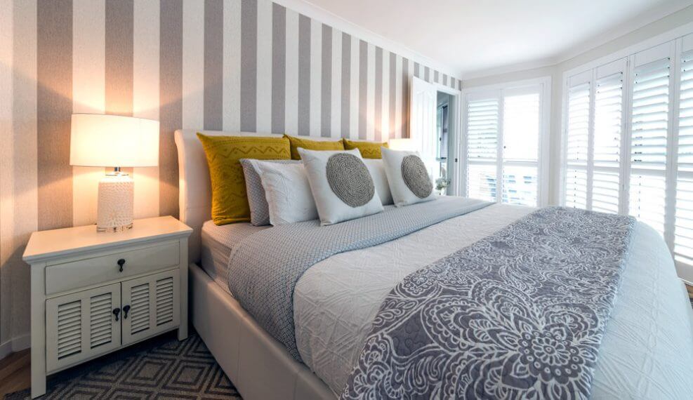 Interior design gold coast bedroom with white and grey striped wallpaper a large bed and a bedside table with a lamp